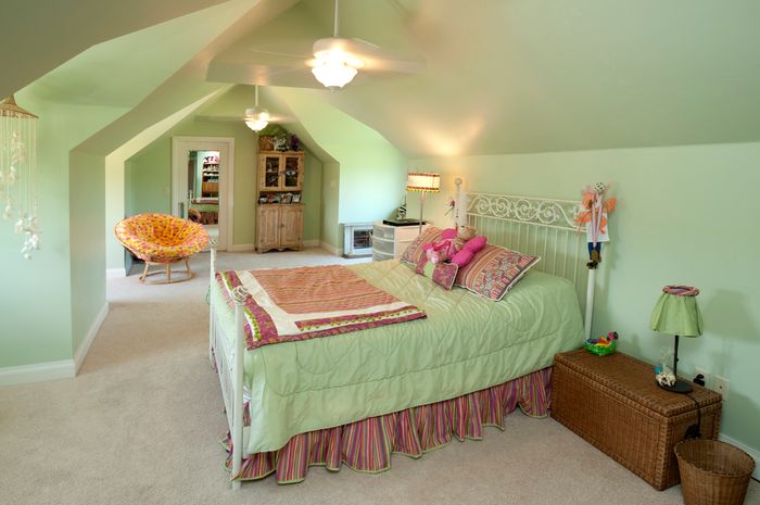 A white-walled bedroom with white comforter, pink pillows, and an orange circle chair.